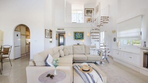 A spacious living room with a high ceiling, a staircase, and a fireplace.