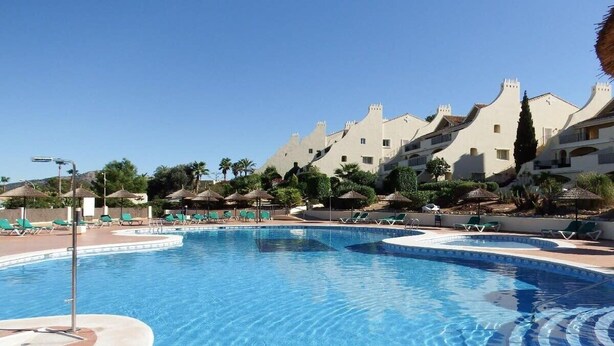A swimming pool with lounge chairs and umbrellas, surrounded by buildings with a unique architectural style.
