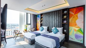 A modern hotel room with two beds, a large window, a city view, a decorative wall, and a small table with a vase.