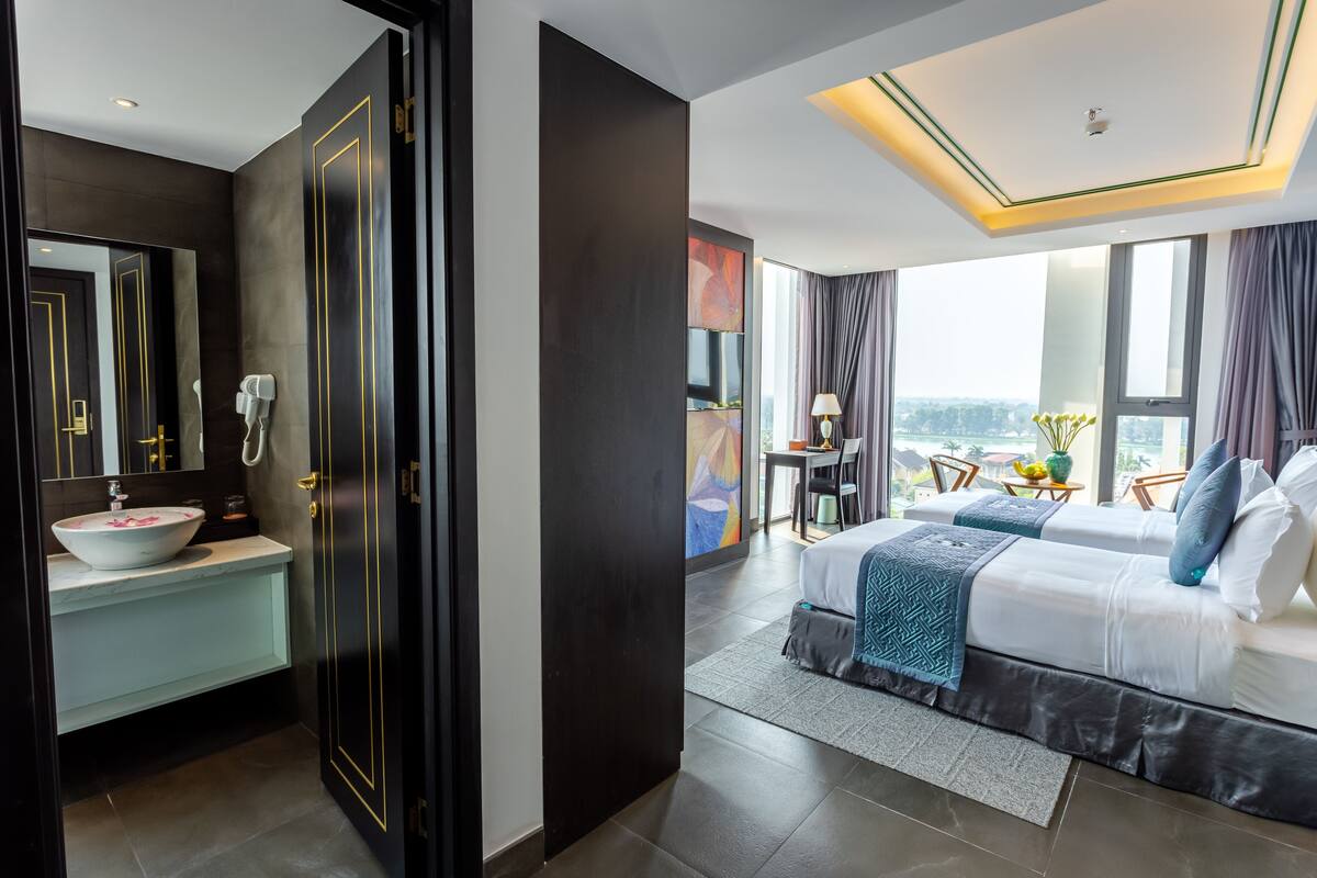 A modern hotel room with a large bed, a bathroom with a sink and mirror, and a view of the city.