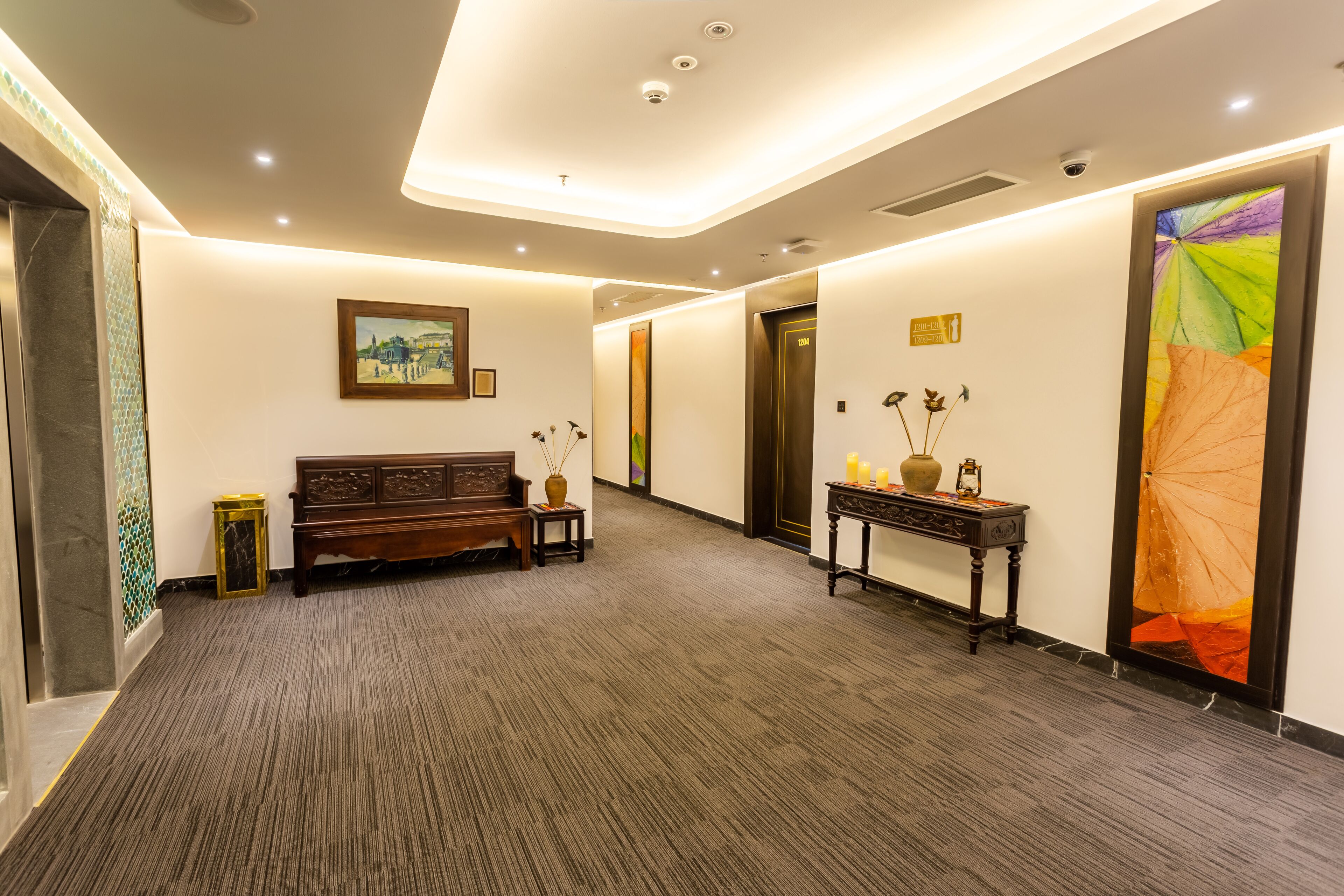 Eine Hotelhalle mit einer hölzernen Bank, einem kleinen Tisch mit einer Vase und einem großen, farbenfrohen Kunstwerk an der Wand.