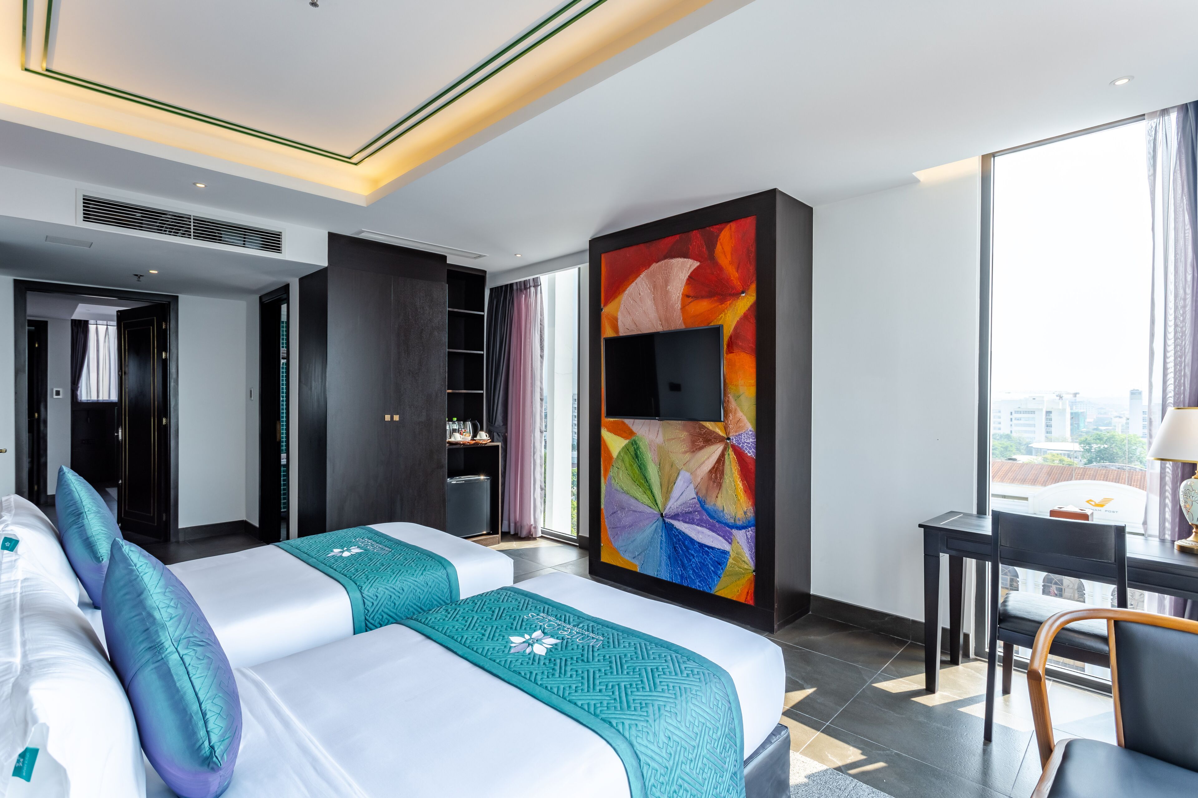 A modern hotel room with a large bed, a desk, and a colorful abstract painting on the wall.