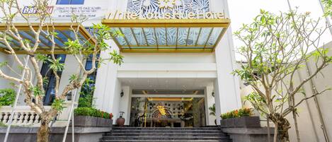 A hotel entrance with a modern facade, a staircase leading up to the entrance, and potted plants on either side.
