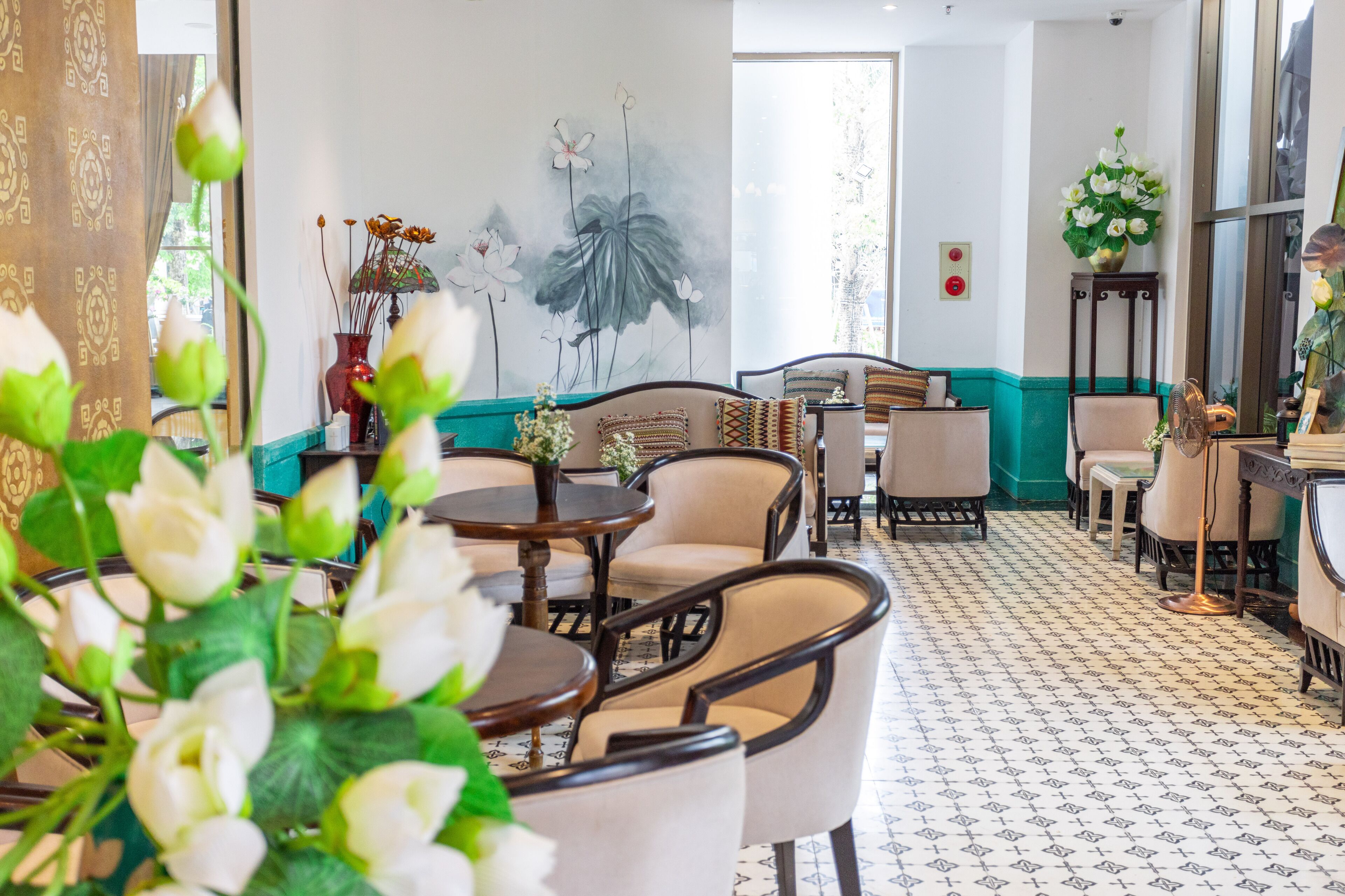 A hotel lobby with round tables, cushioned chairs, a large wall mural, and a patterned floor.