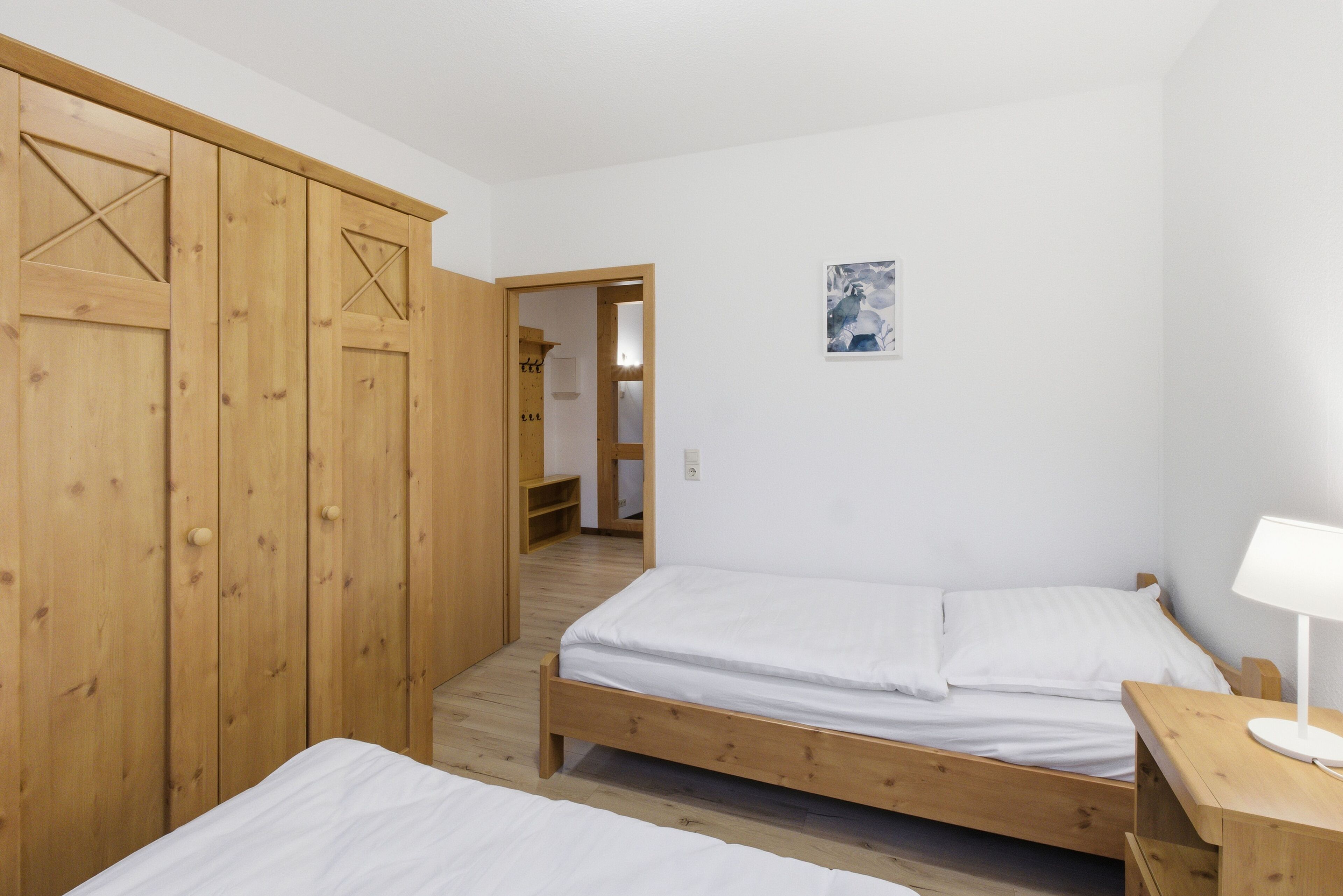 A bedroom with two wooden beds, a wooden wardrobe, and a small bedside table with a lamp.