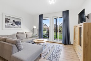 Un salon moderne avec un canapé gris, une petite table ronde et un téléviseur posé sur un meuble en bois.