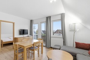 Une pièce moderne et bien éclairée, avec une table à manger en bois, des chaises, un canapé, un téléviseur et une fenêtre avec des rideaux.
