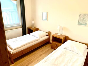 A small, clean room with two single beds, a window, a radiator, and a nightstand with a lamp. - Haus Karola Ferienwhg. 1 - Vineta Ferienwohnungen GbR (Mölschow)