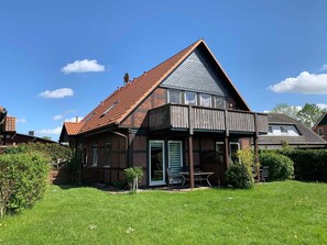 Ein zweistöckiges Haus mit geneigtem Dach, einer Holzterrasse und einem kleinen Garten.