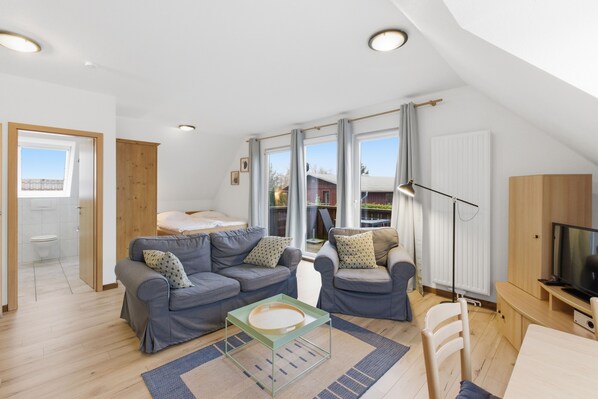 Ein modernes Wohnzimmer mit zwei grauen Sofas, einem Glastisch und einer TV-Konsole aus Holz.