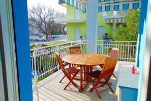 Un balcone con un tavolo e sedie in legno tondo, una ringhiera bianca e vista su un edificio verde.