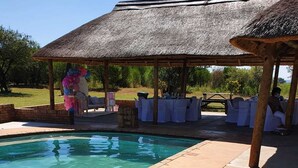 Un área de piscina con un pabellón de techo de paja, sillas de descanso y una mesa lista para un evento.