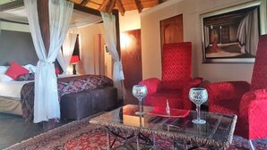 Una habitación con una cama, un sofá rojo, una mesa de centro de cristal y un cuadro en la pared.