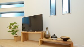 Ett minimalistiskt vardagsrum med en platt-TV på ett träställ, ett litet bord med dekorativa skålar och en krukväxt.
