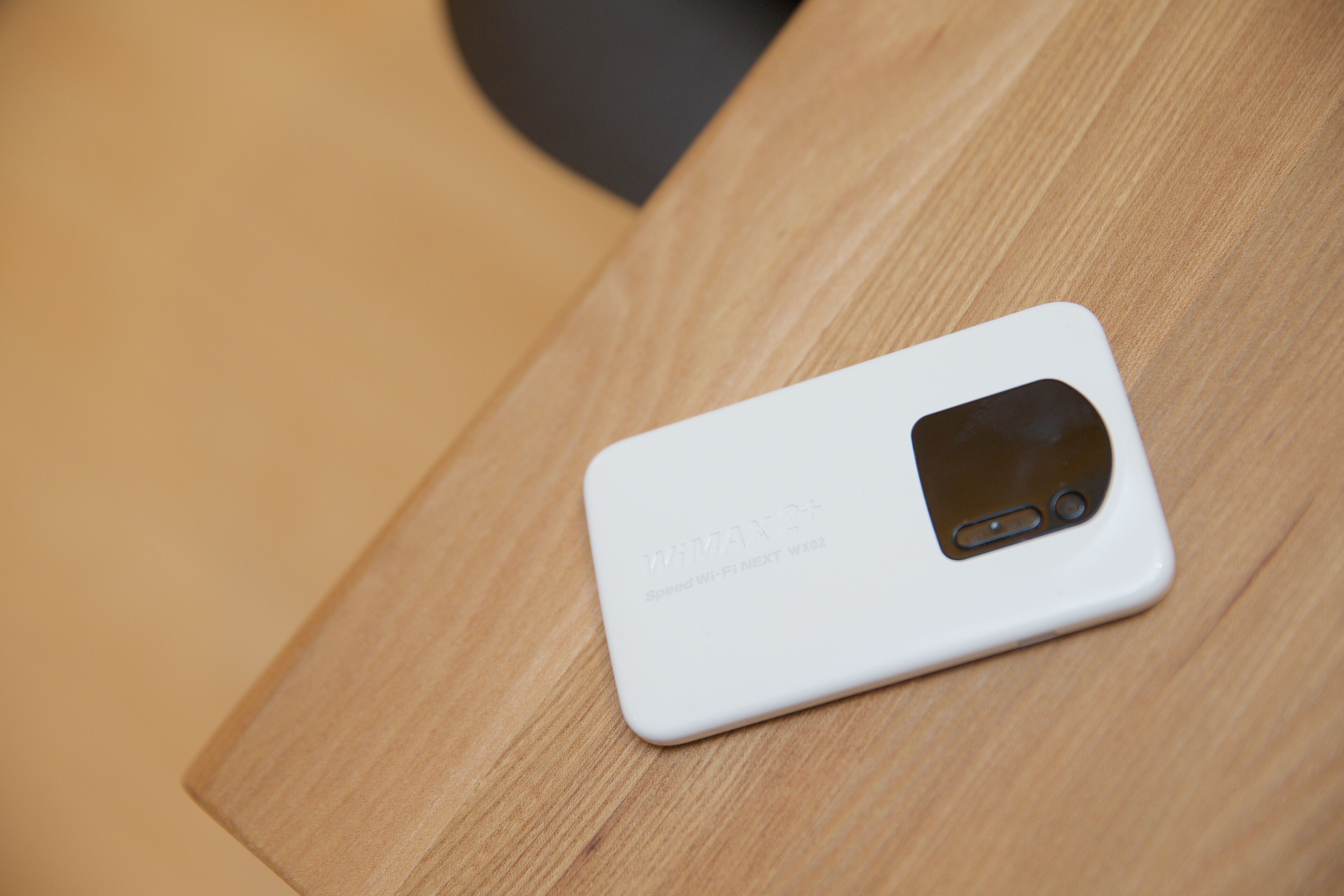 A white smartphone with a camera and a logo on a wooden surface.