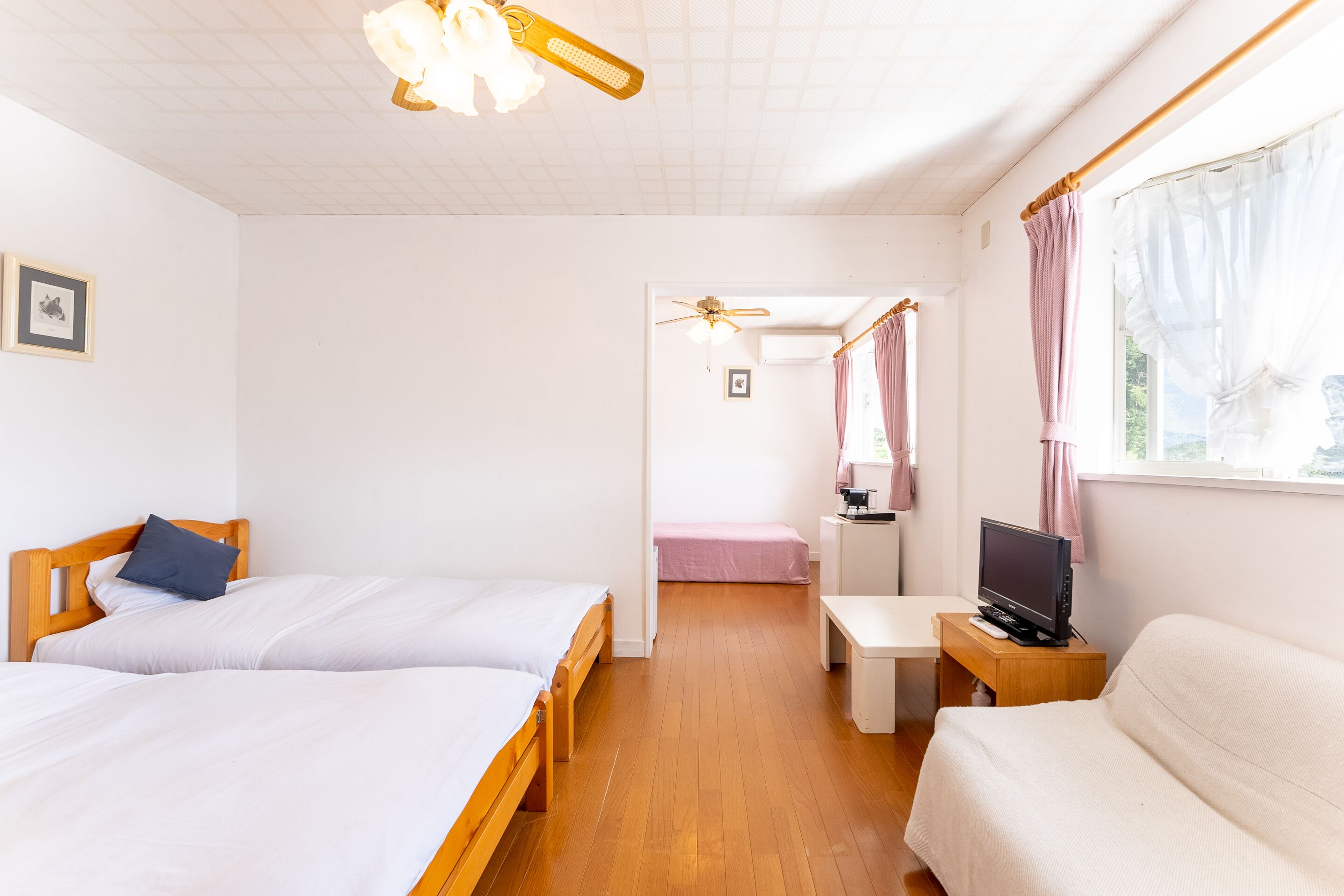 A hotel room with two beds, a TV, a desk, and a window with curtains.