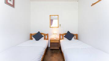 Une chambre avec deux lits simples, une table de chevet avec une lampe, un tableau encadré au mur et une poutre en bois au plafond.