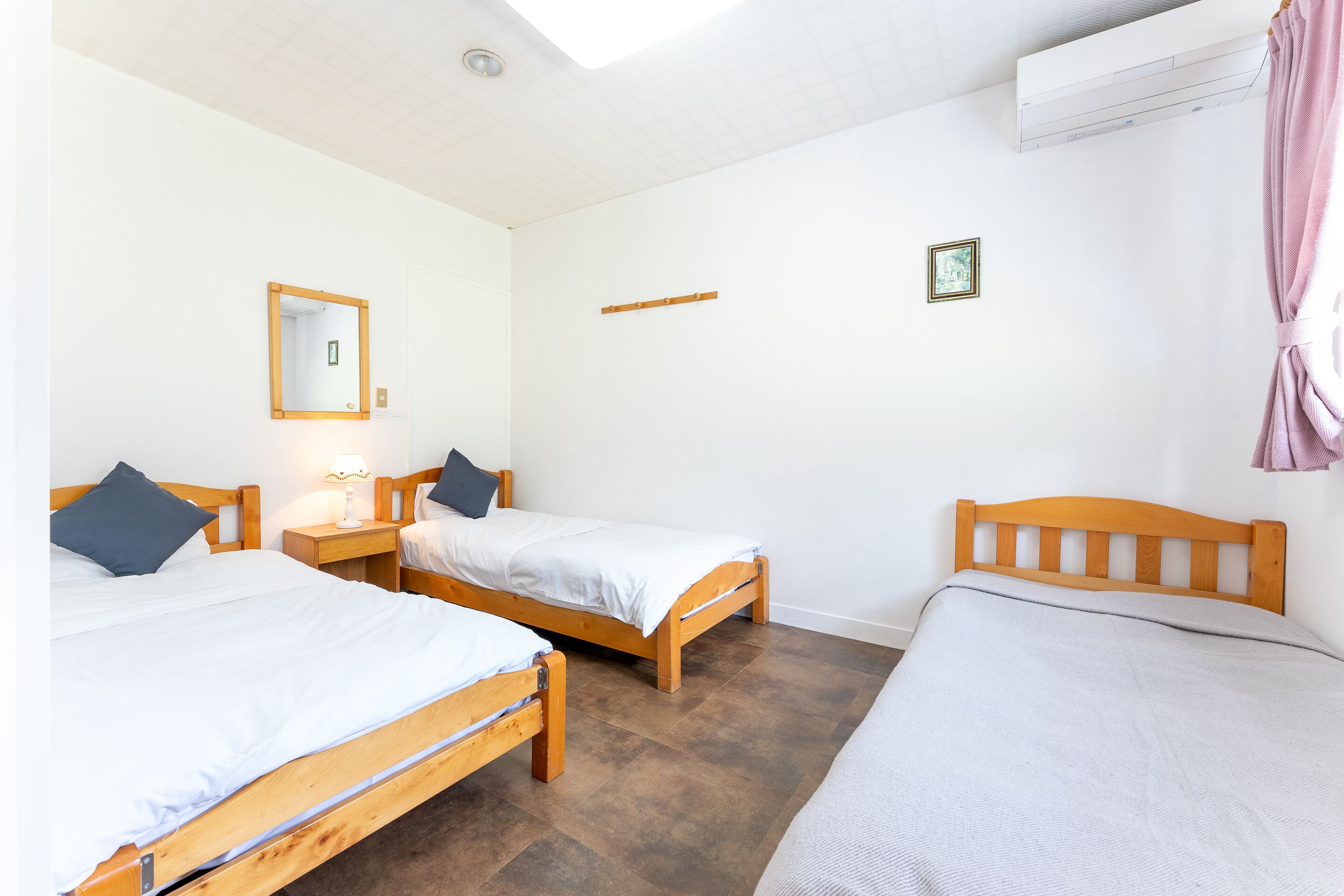 Una habitación con dos camas de madera, un espejo, un pequeño estante y un equipo de aire acondicionado.