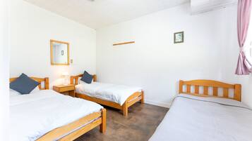 Una habitación con dos camas de madera, un espejo, un pequeño estante y un equipo de aire acondicionado.