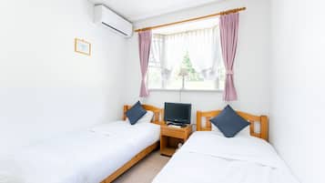 Ein Schlafzimmer mit zwei Einzelbetten, einem Nachttisch aus Holz mit Fernseher und einem Fenster mit Vorhängen.