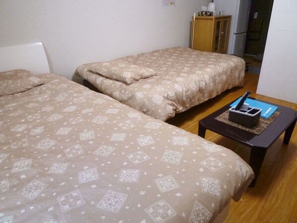A room with two beds, a small table with a coffee maker, and a cabinet.