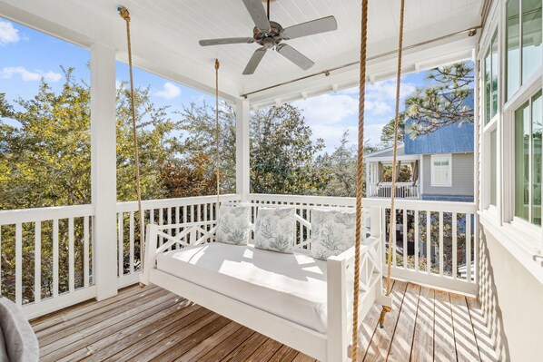 A covered porch with a white swing seat and a ceiling fan.