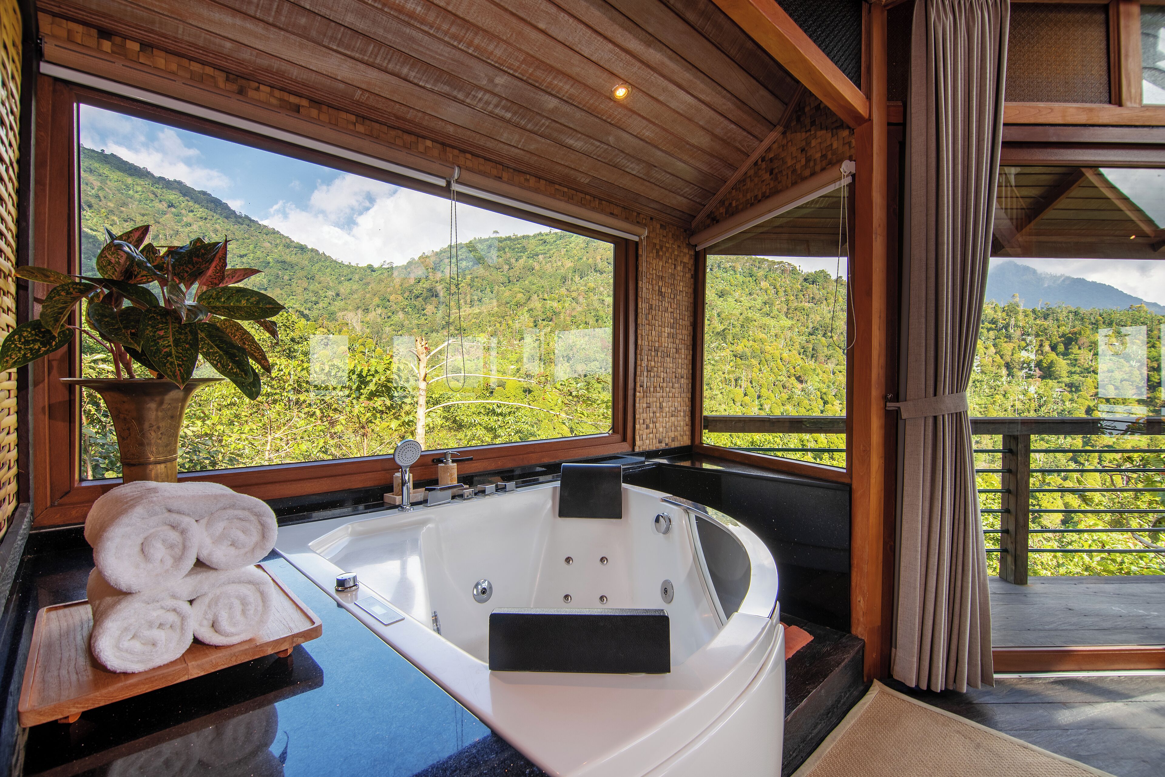 A spa room with a large bathtub, a wooden bench, and a view of a mountainous landscape.