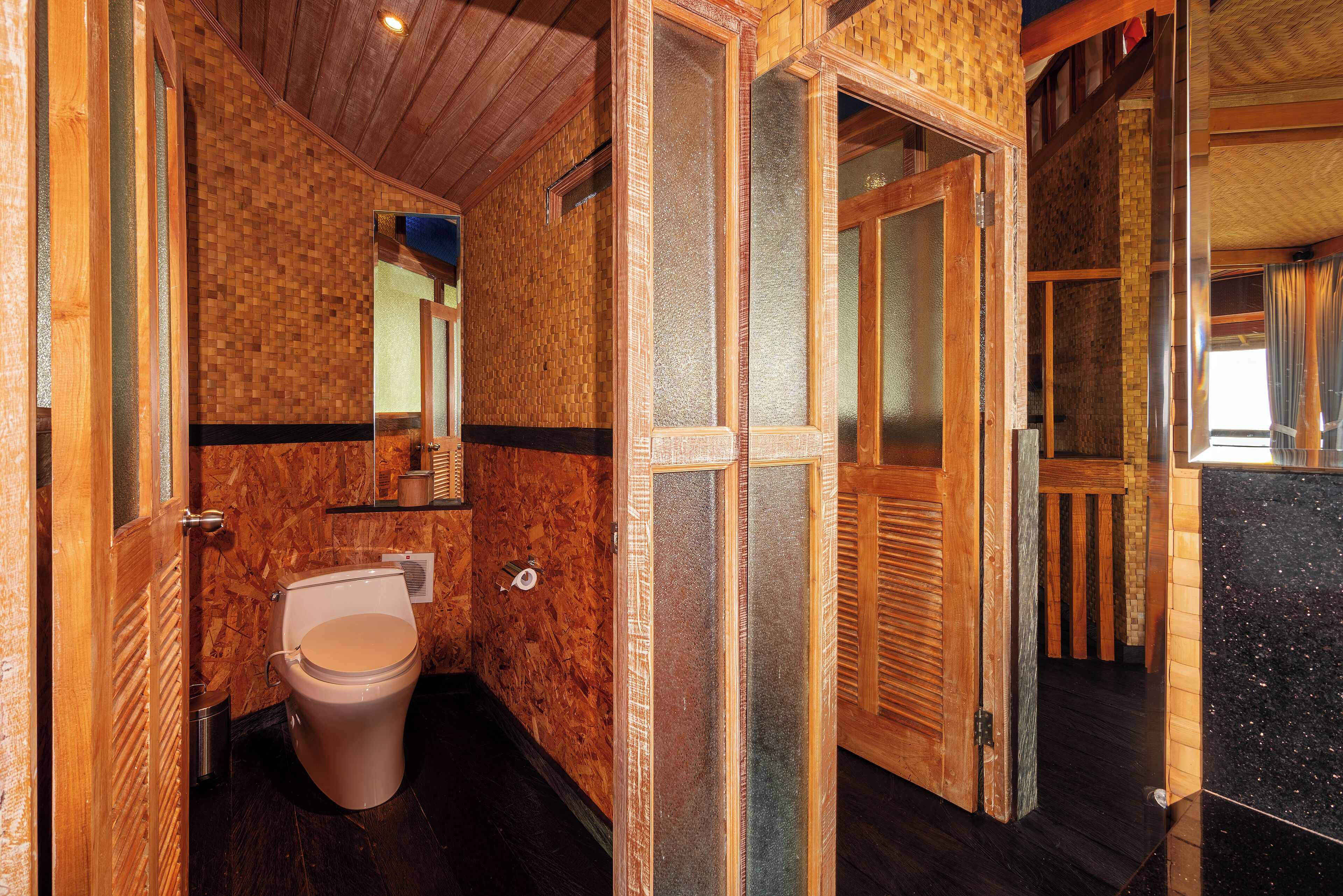 A wooden interior with a toilet, a mirror, and a door leading to another room.