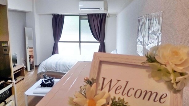 Quarto de hotel com cama, escrivaninha, televisão e placa de 'Welcome'.
