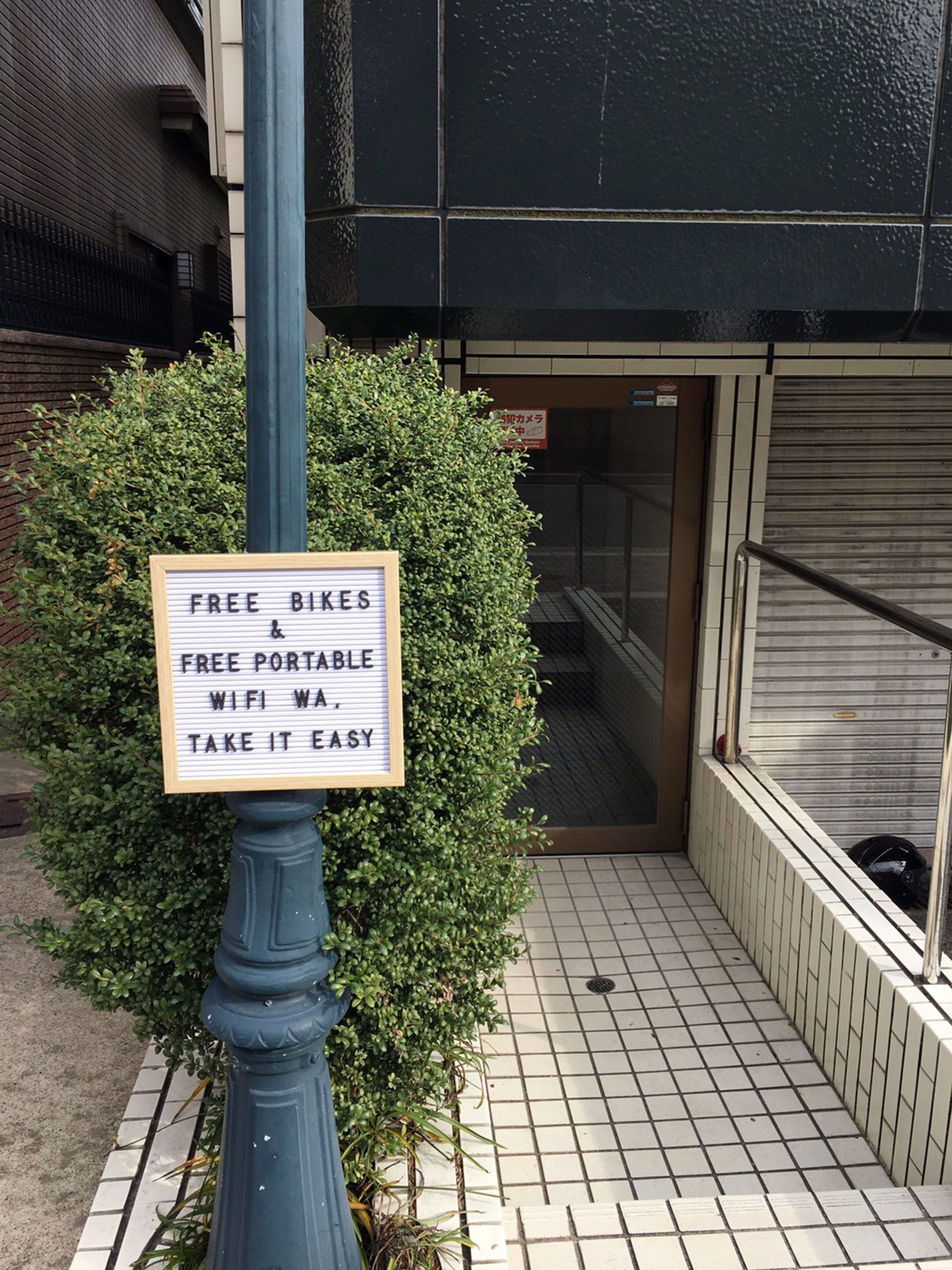 A sign offering free bikes and portable WiFi, placed on a pole beside a building entrance.