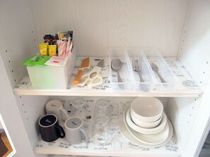 A kitchen with a white shelf containing various items like a box of tea bags, a pair of scissors, and utensils. Below, there are mugs and plates on another shelf. - Free bike & free WIFI 301 Take it easy (Kyoto)
