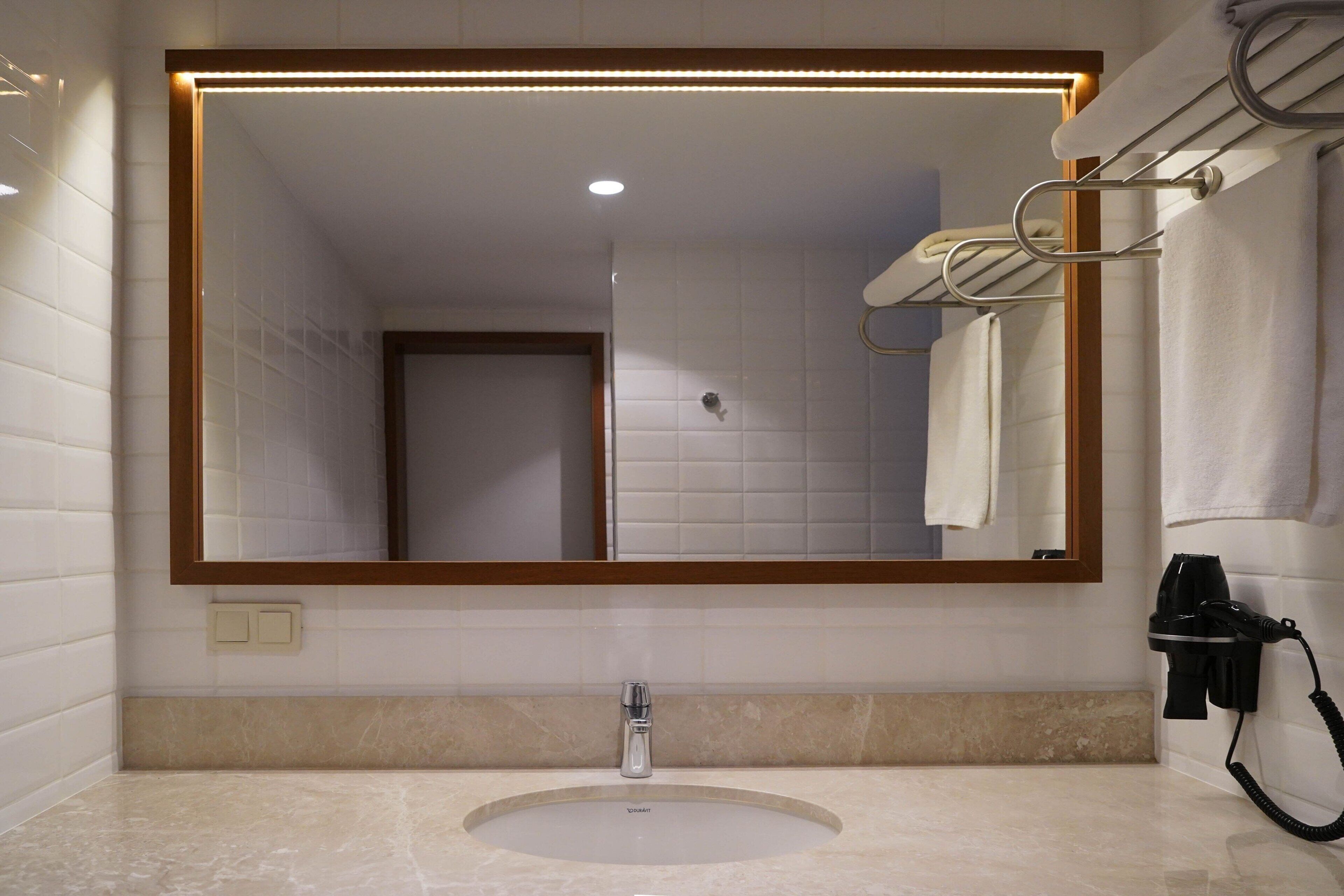 A bathroom with a large mirror, a sink, and a towel rack.