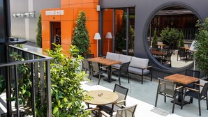 An outdoor seating area with tables and chairs, surrounded by potted plants and a modern building with an orange facade. - Four Points Flex by Sheraton Bursa Nilüfer  (Bursa)