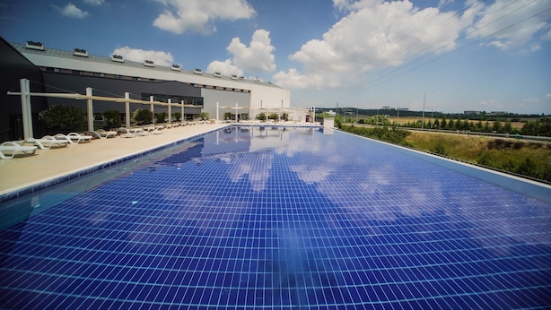 A swimming pool with a tiled deck and lounge chairs, a building with a flat roof and multiple windows, and a clear sky with scattered clouds. - Four Points Flex by Sheraton Bursa Nilüfer  (Bursa)