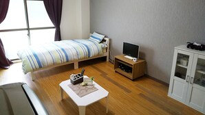 Una habitación pequeña y ordenada con cama, televisor sobre un mueble, una mesita con un cartel de bienvenida y un armario.