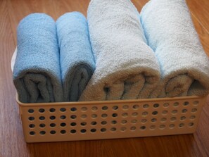 A beige basket with perforated sides containing rolled towels in shades of blue and white.