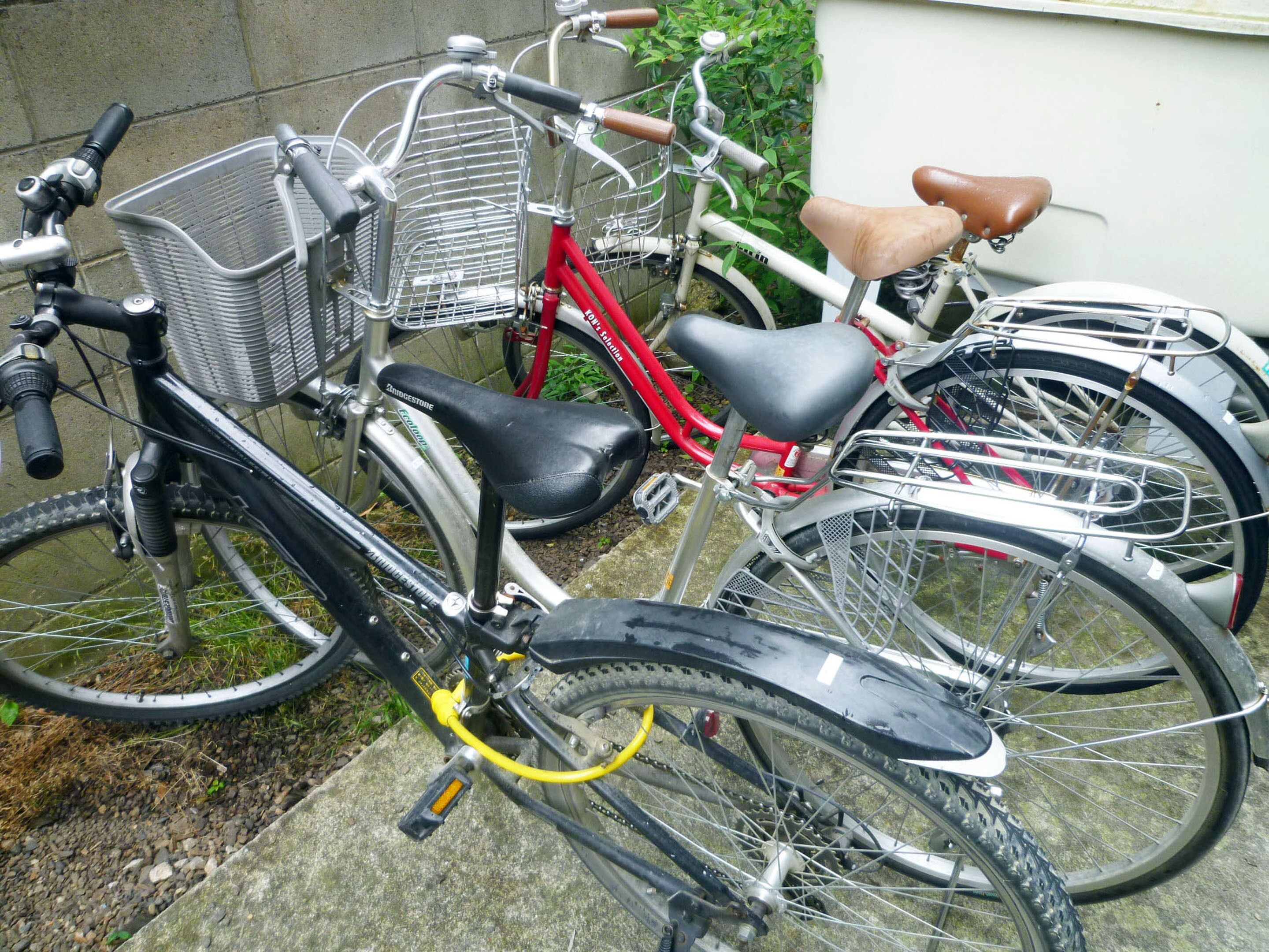 A row of bicycles parked against a wall, with a basket attached to one and a bell on another.