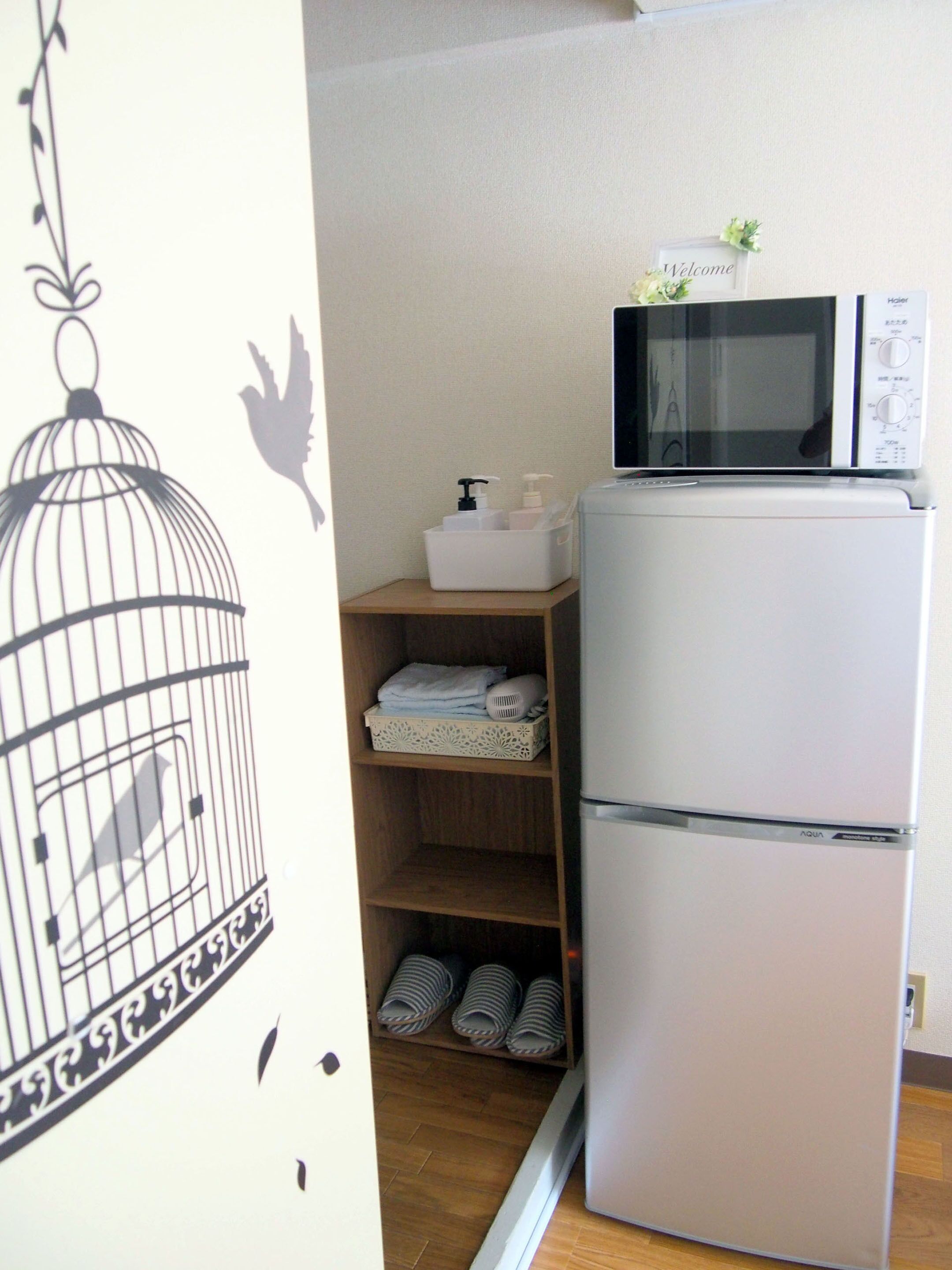 A kitchen with a white refrigerator, a microwave, and a wooden shelf with folded towels and a basket.