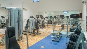 Ein Fitnessstudio mit verschiedenen Trainingsgeräten, Spiegeln und zwei Bildschirmen an der Wand.