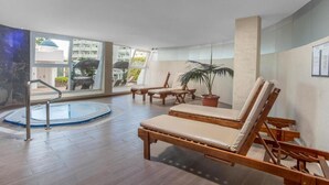 Ein großzügiger Innenbereich mit Holz-Loungemöbeln, einem kleinen Pool und großen Fenstern mit Blick ins Freie.