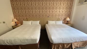 A hotel room with two beds, a patterned wallpaper, bedside lamps, and a carpeted floor.