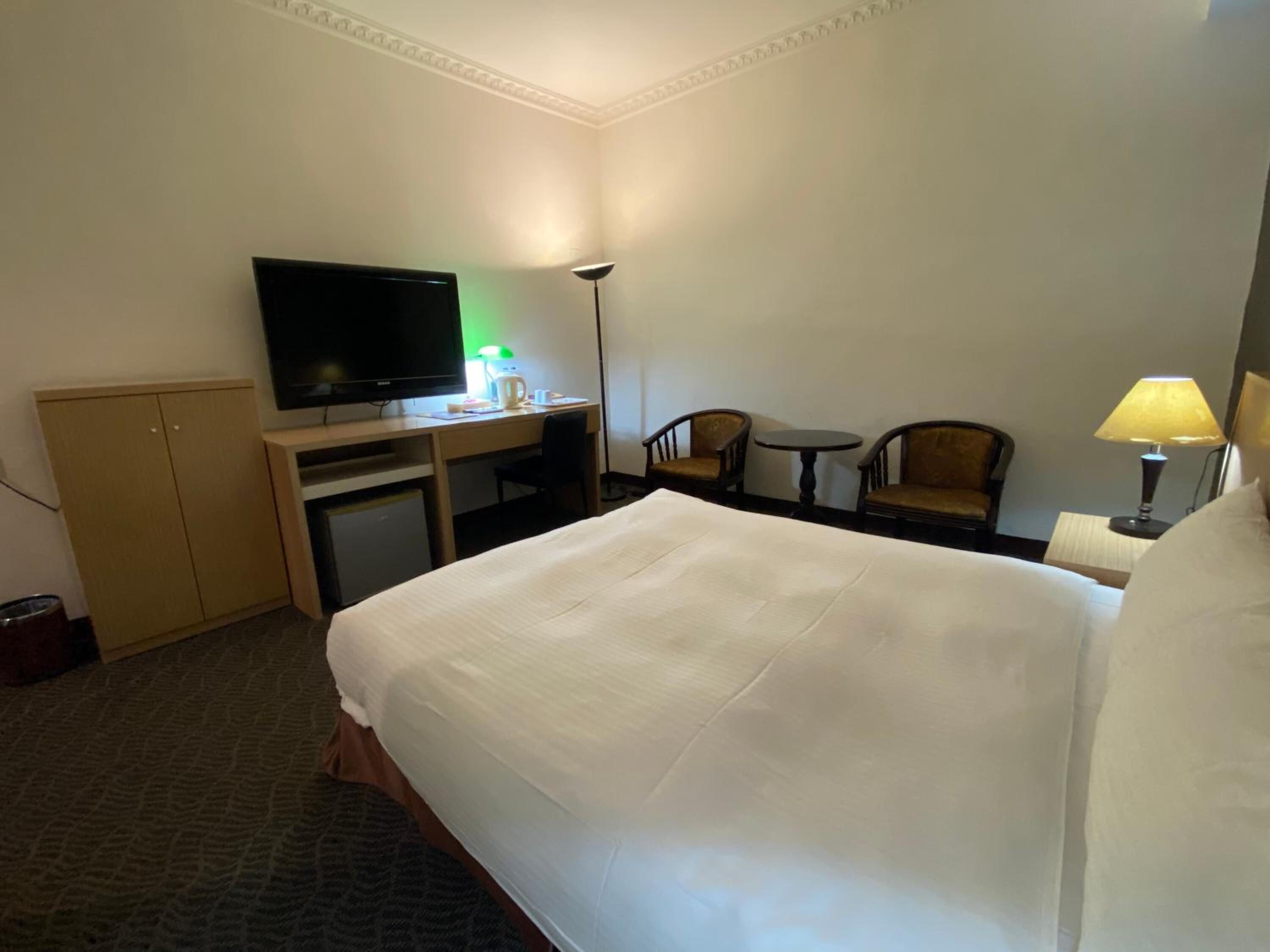 Une chambre d’hôtel avec un grand lit, un bureau avec une télévision, une chaise, une petite table et une lampe.