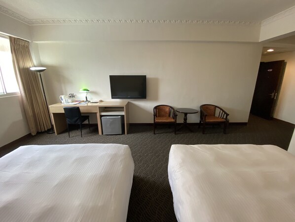 A hotel room with two beds, a desk with a computer, a small fridge, a TV, and two chairs.