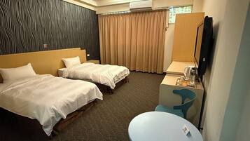 A hotel room with two beds, a desk with a chair, a small table, an air conditioning unit, and a television.
