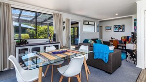A modern living room with a glass dining table, white chairs, a sofa, and a television.