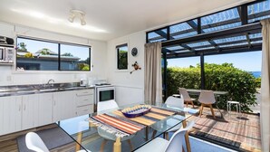 A modern kitchen with a glass dining table, white cabinets, and a view of the sea.