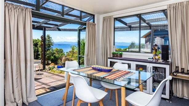 A modern dining area with a glass table, white chairs, and a view of the sea.