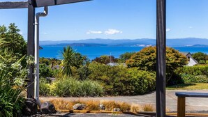 A view from a covered outdoor area with a bench, lush greenery, and a distant view of the sea and mountains.