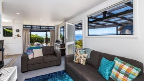 A modern living room with two sofas, a TV, and a large window with a view of greenery and mountains.