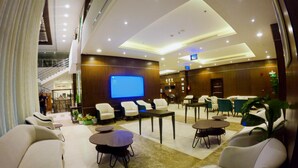 A modern hotel lobby with a large screen, comfortable seating, and a staircase in the background. - Beyab Al Azizeyyah Hotel (Makkah)